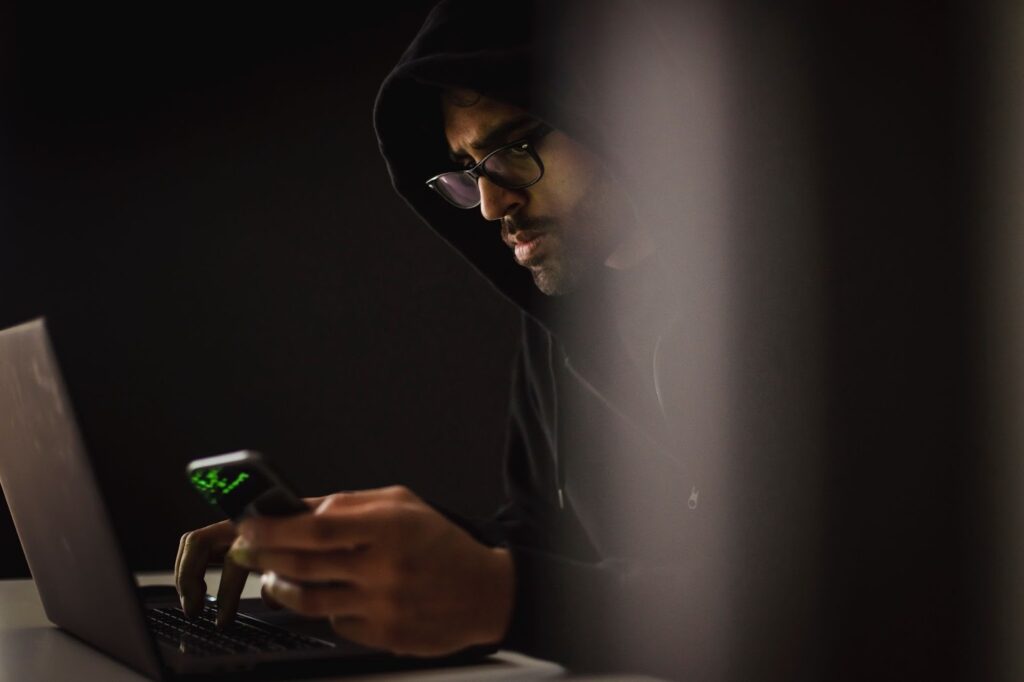 man in black hoodie using phone and laptop